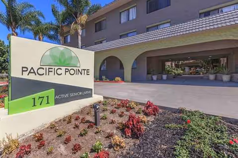 Front exterior of Pacific Pointe senior living with sign, arches, and palm trees.