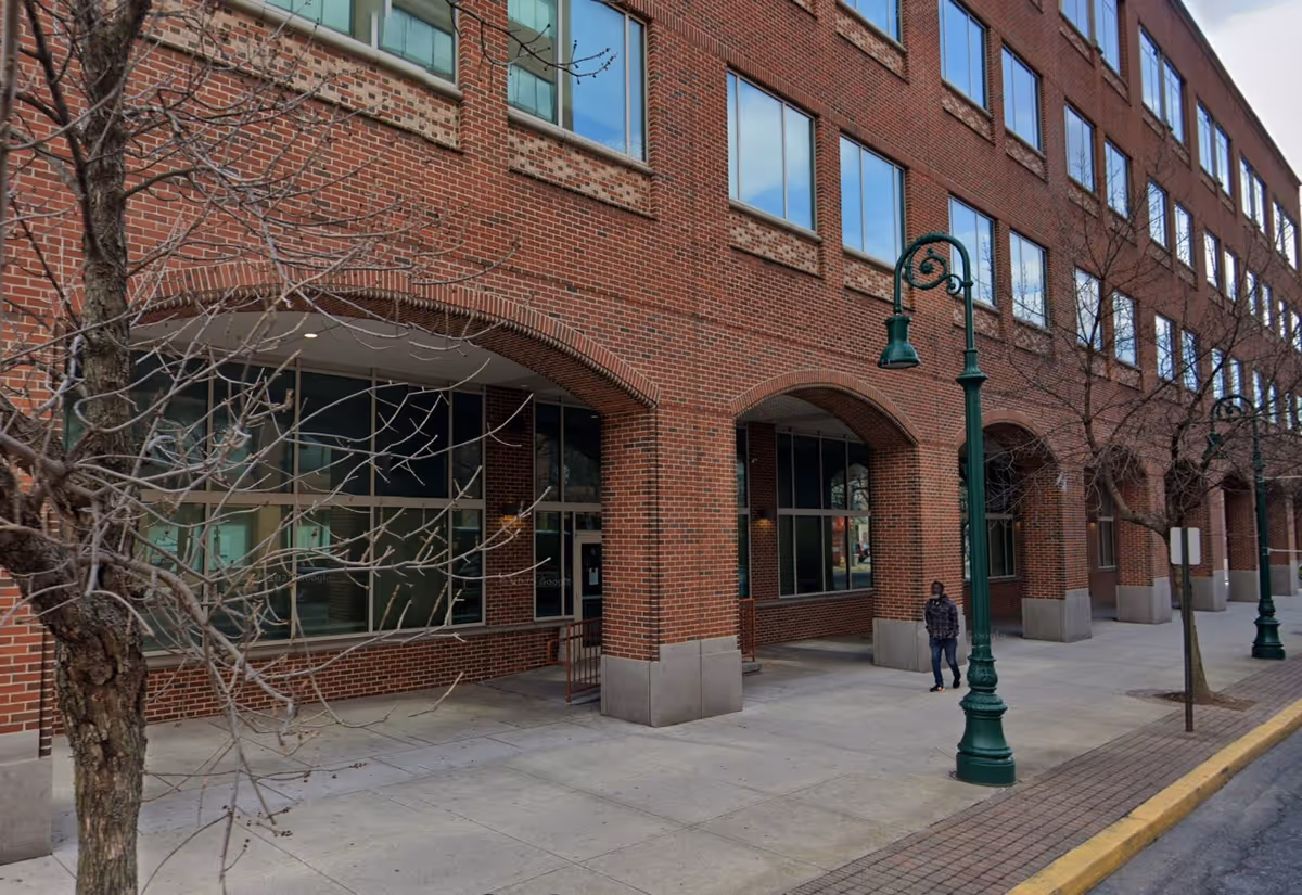 Brick building with arches along a sidewalk and a lone pedestrian.