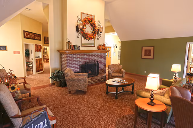 Cozy senior living lounge with a brick fireplace, comfortable seating, and small side tables.