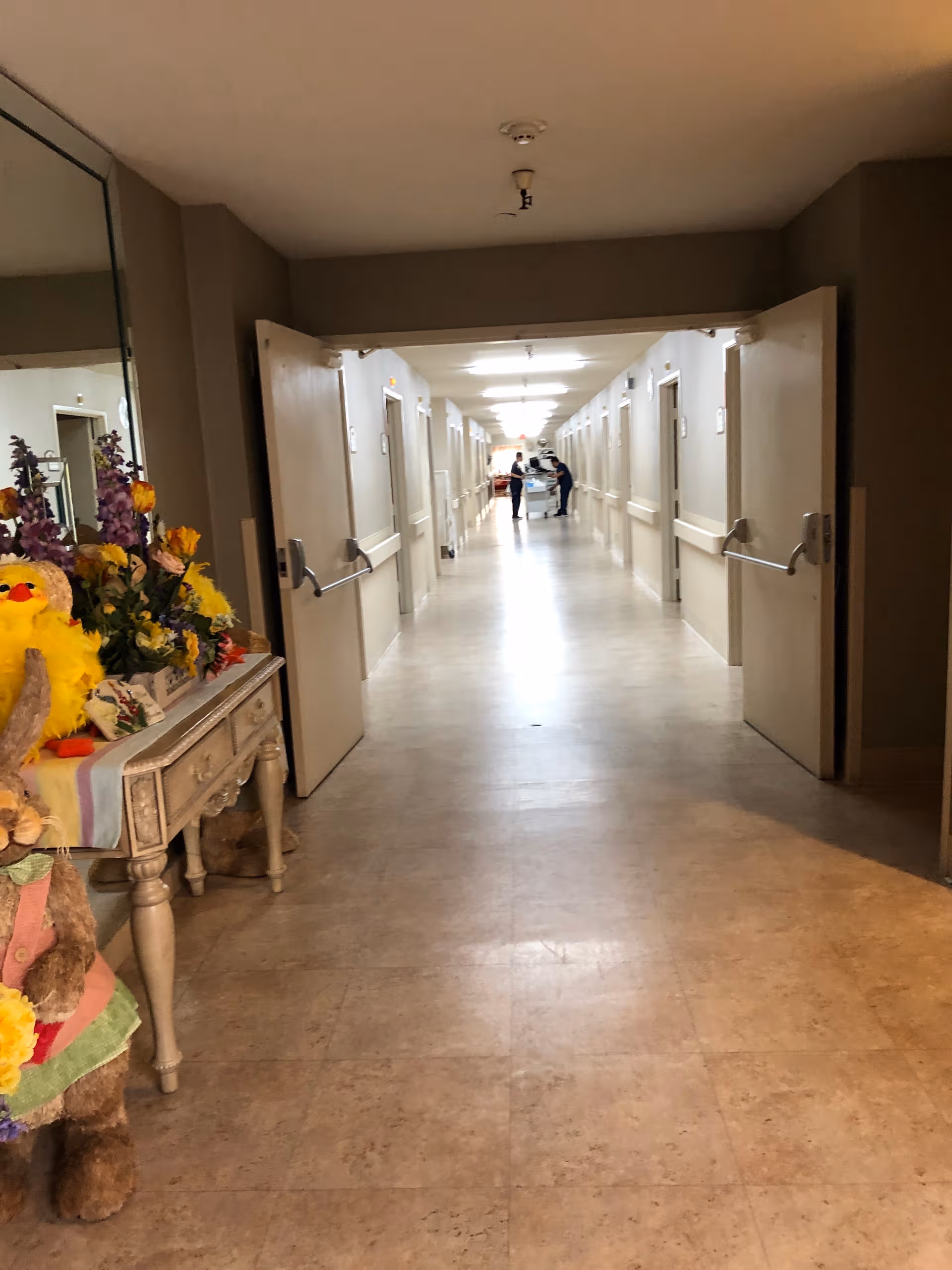 Long hospital hallway with doors on both sides and a floral display in the foreground