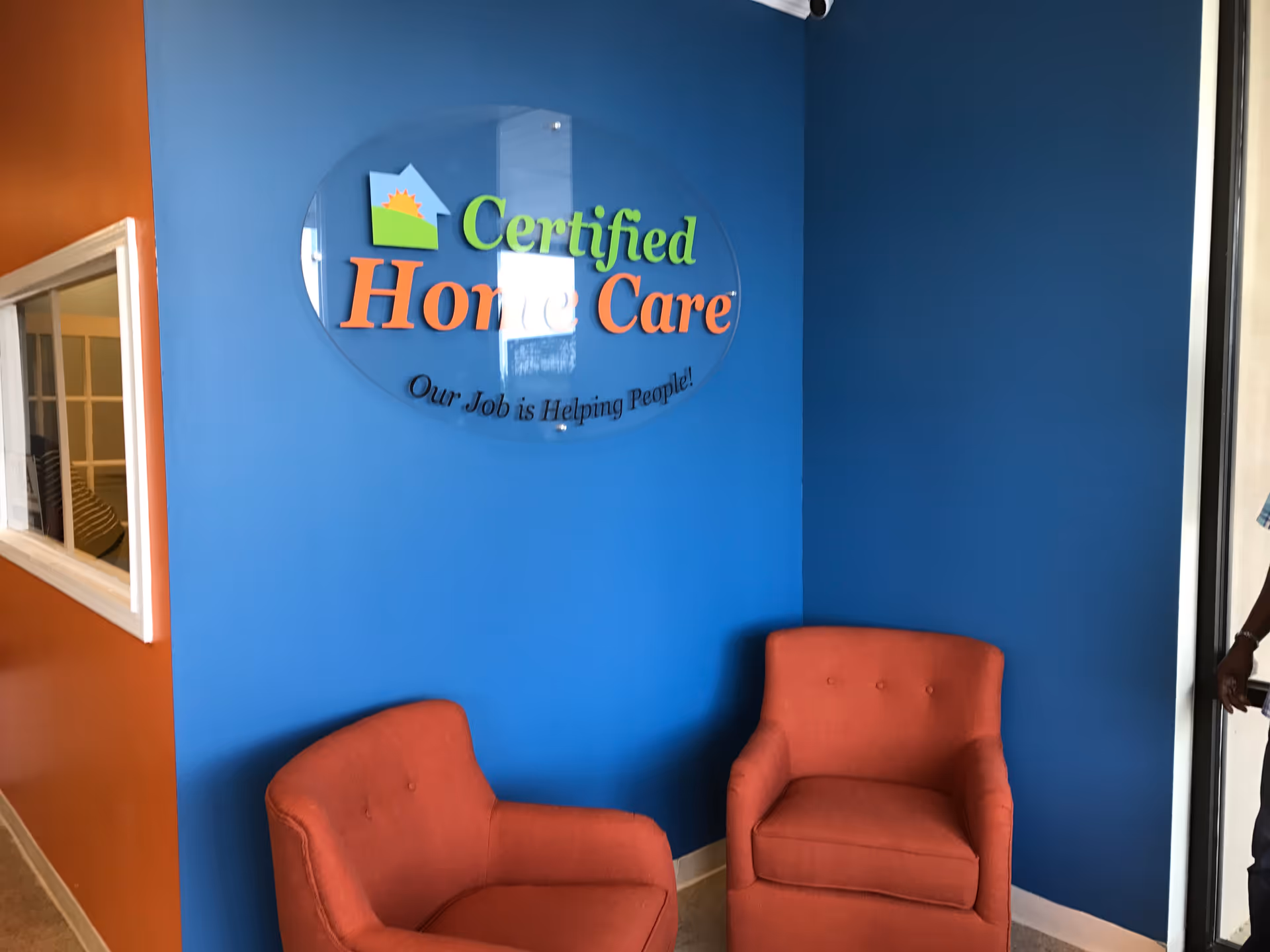 Blue interior lobby with a circular Certified Home Care sign and orange chairs.