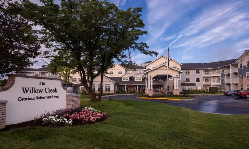 Front exterior of Willow Creek Gracious Retirement Living with a landscaped lawn, entrance canopy, and a sign in the foreground.