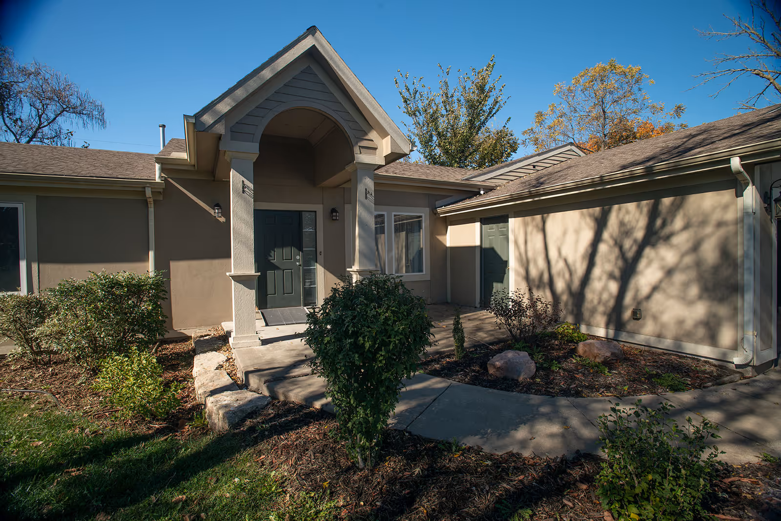 Single-story senior living building with a covered entry and landscaped front walkway.