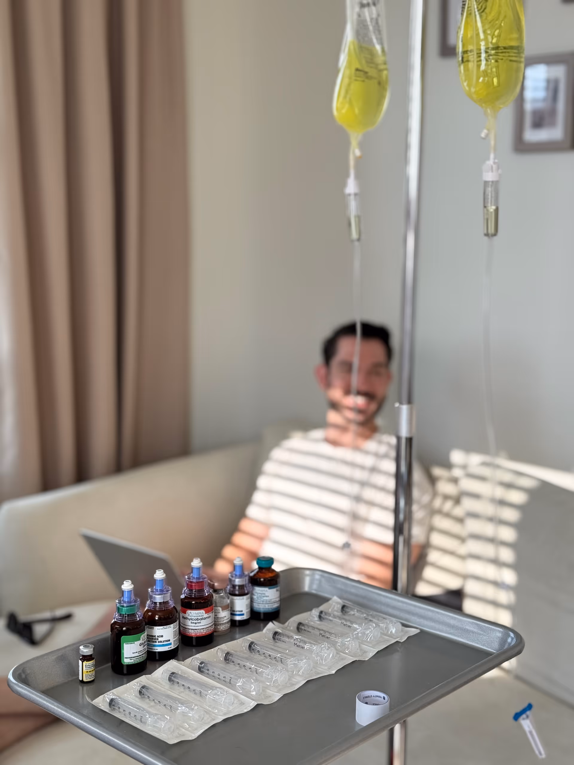 IV drip bags and medication tray in foreground, resident on couch in background.