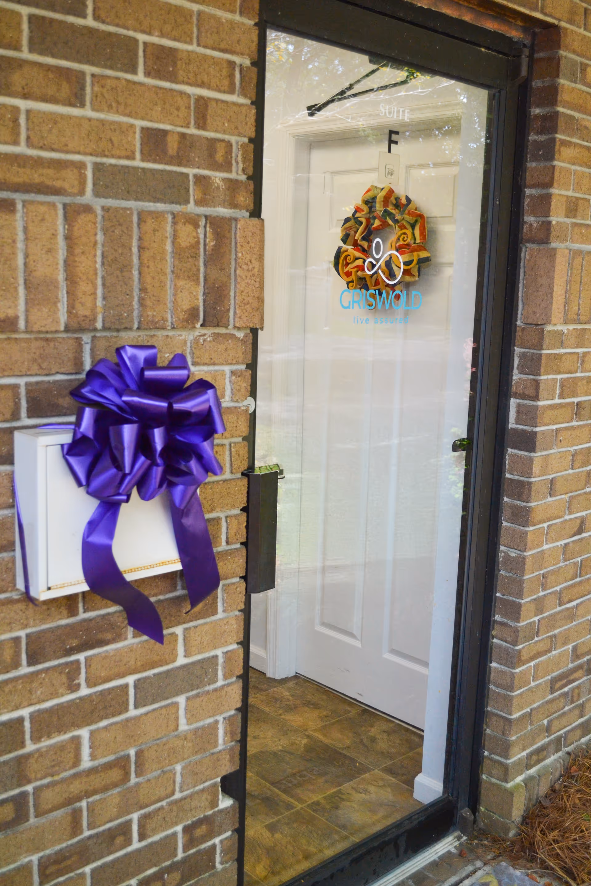 Brick exterior doorway with a purple bow on a mailbox beside a wreath on the door.