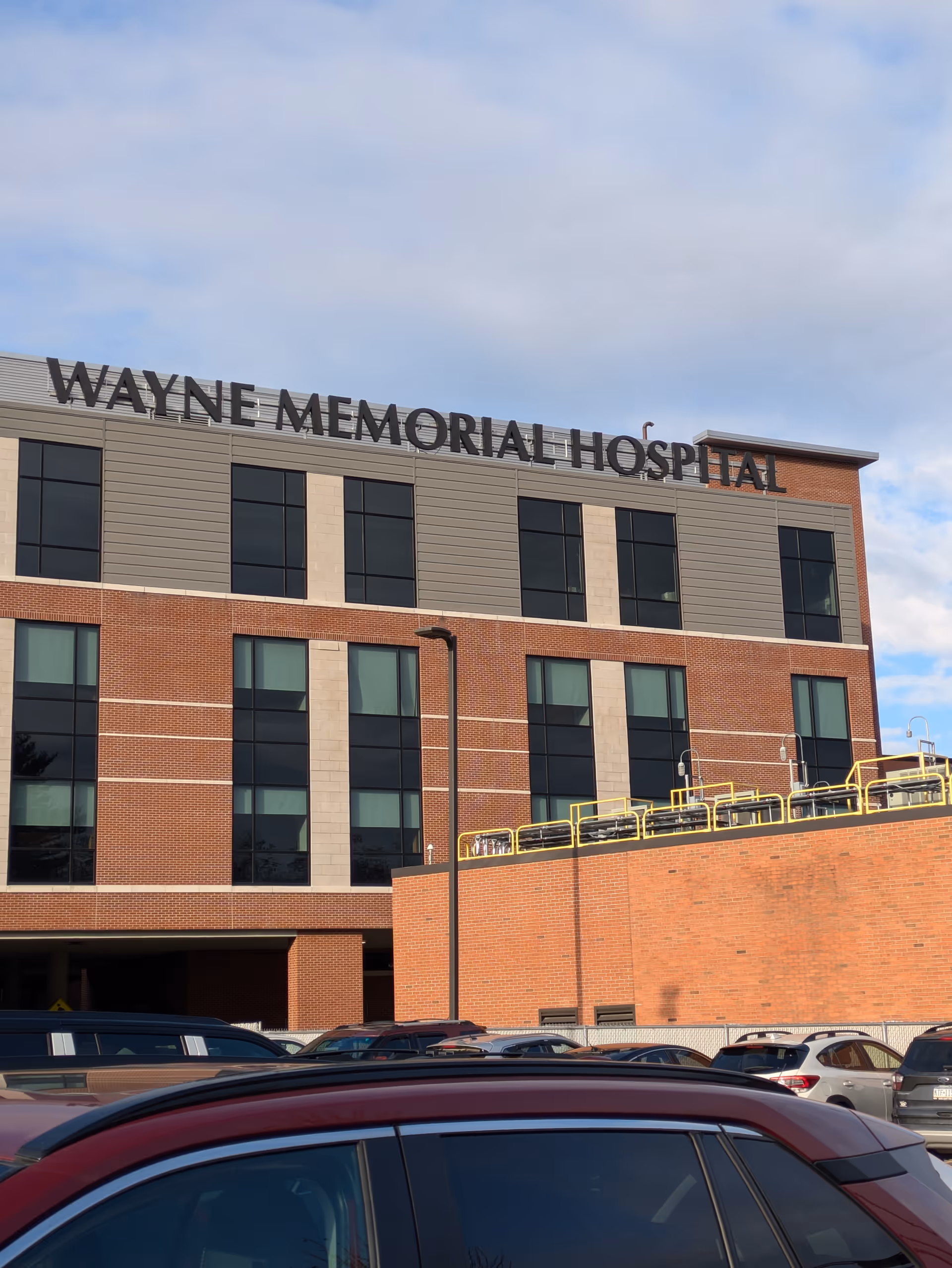 Front exterior view of Wayne Memorial Hospital with parked cars in the foreground.