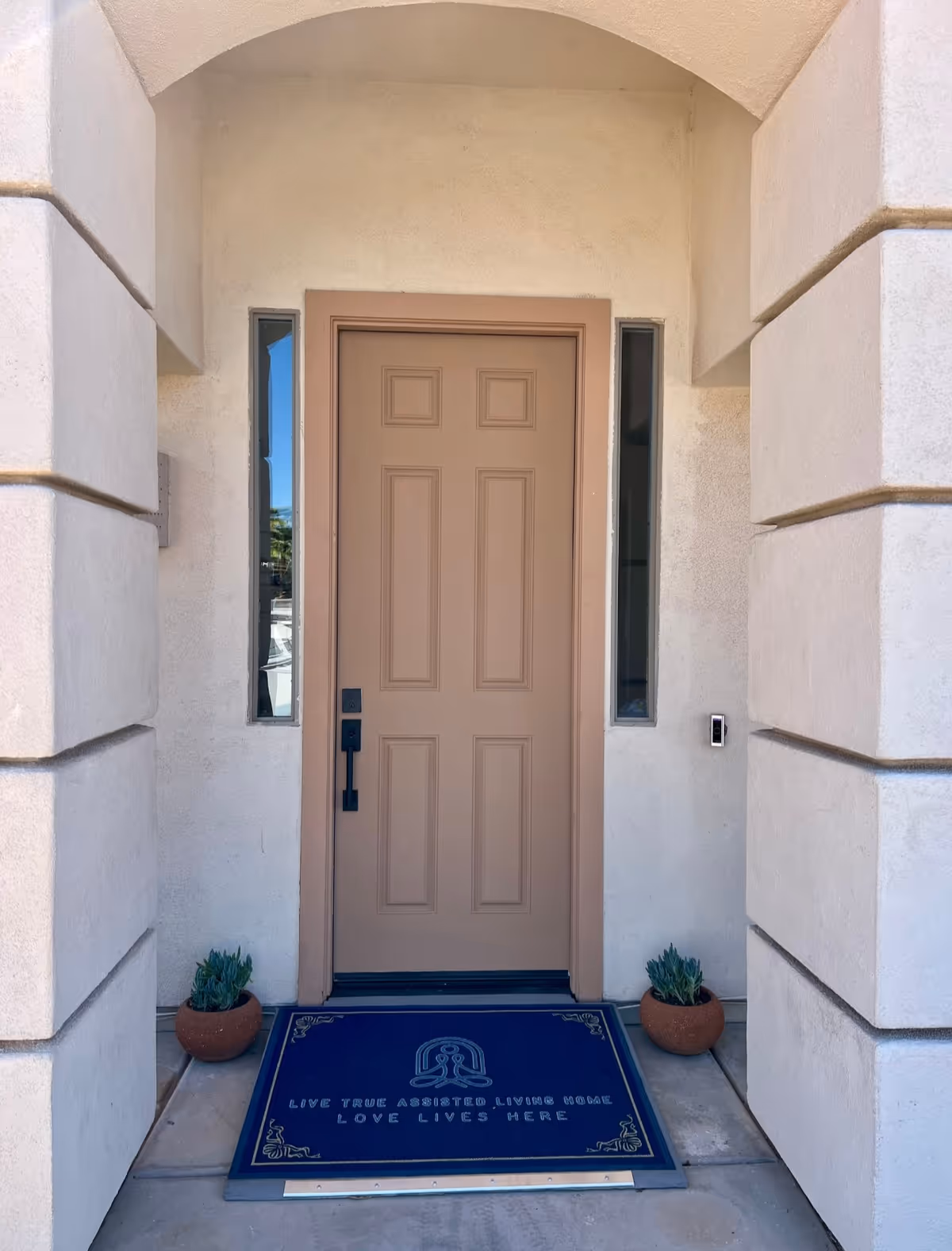 Entrance door to Horizon Manor I with side windows, potted plants, and a welcome mat.