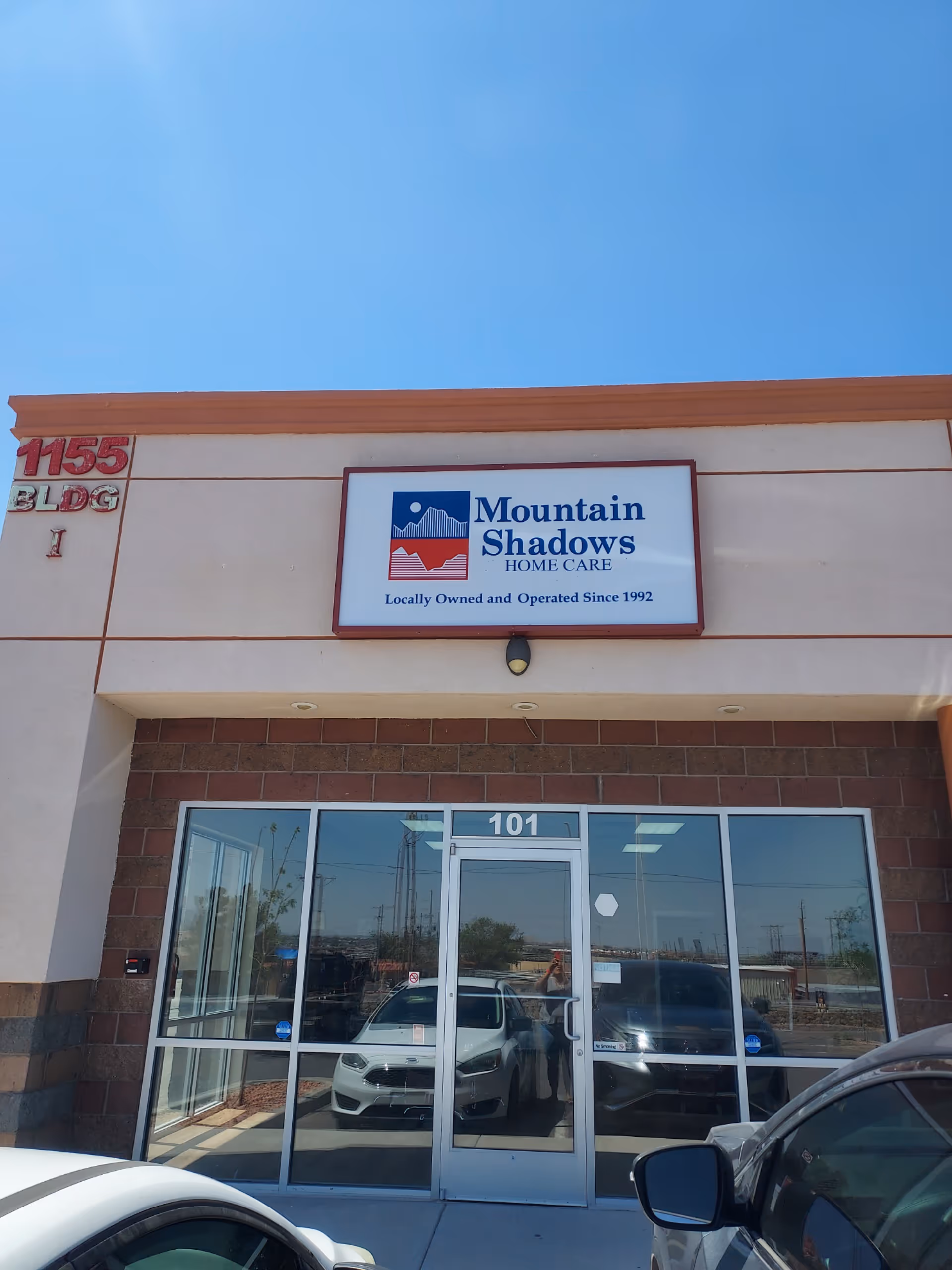 Front view of Mountain Shadows Home Care building with glass entry doors and parked cars