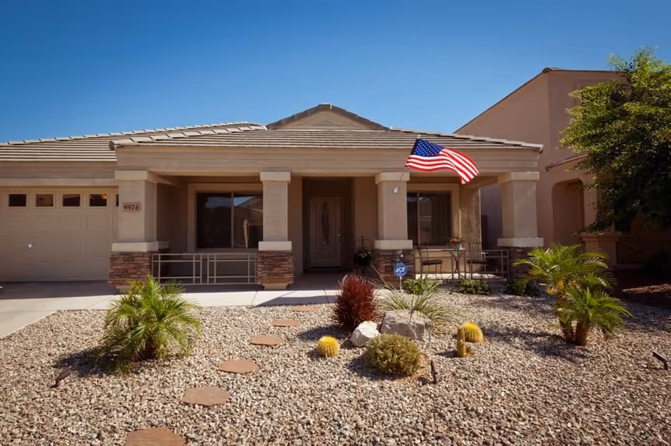 Front view of a single-story assisted living home with flag and desert landscaping.