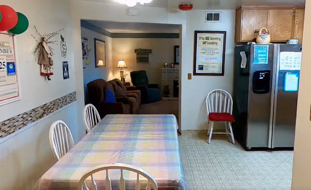 Common dining area with plaid table, white chairs, and a seating lounge in the background.