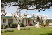 Exterior view of Blythe Post Acute facility with a lawn, blossoming trees, and outdoor seating.