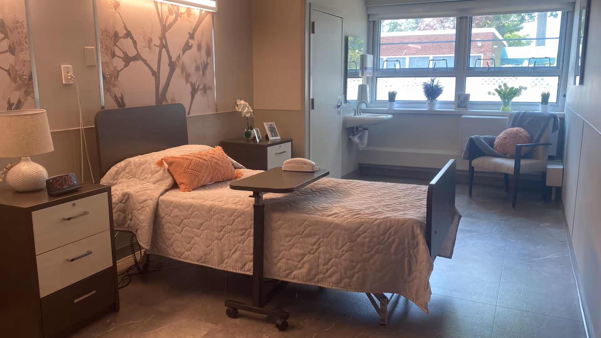 Hospital-style resident bedroom with a bed, nightstands, and a window seating area.