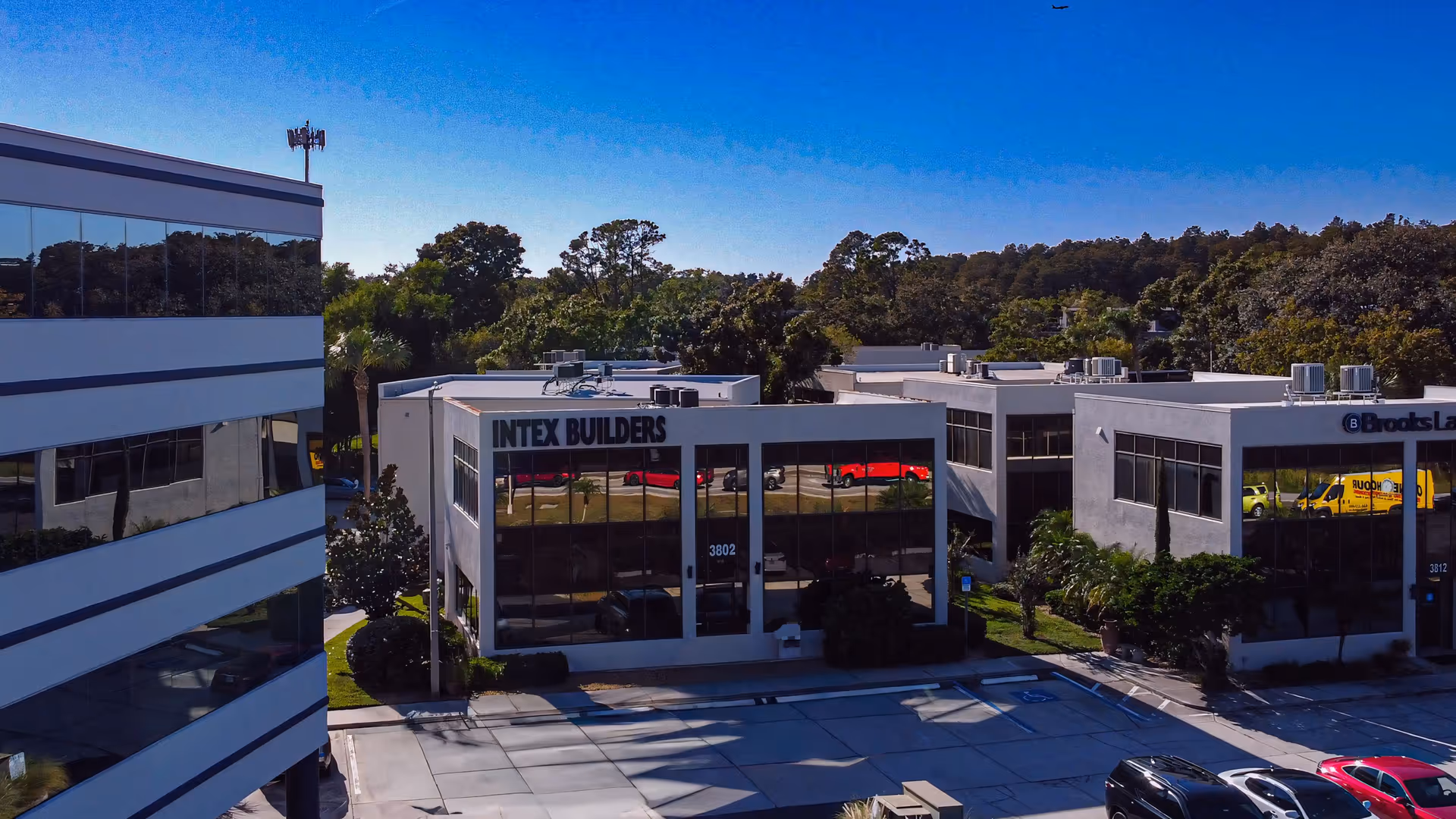 A modern office campus with glass-front buildings and parked cars under a clear blue sky.