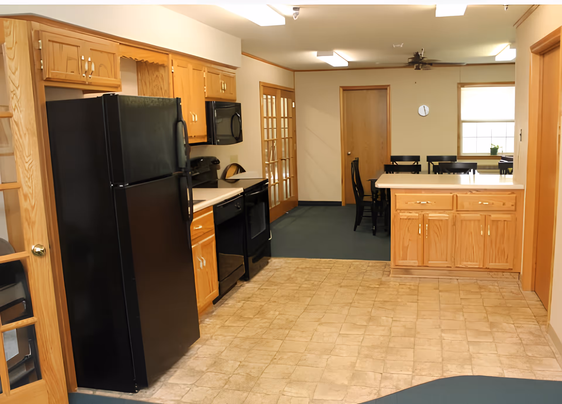 A kitchen with black appliances, oak cabinets, a countertop island, and an adjacent dining area with tables and chairs.
