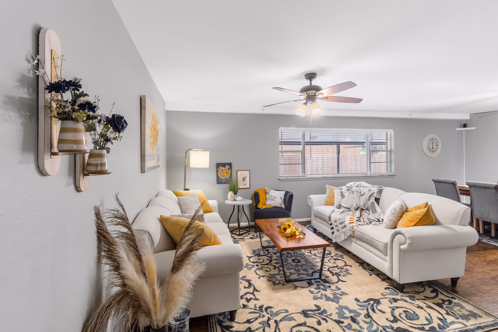 Bright living room with white sofas, a wooden coffee table, and a ceiling fan.