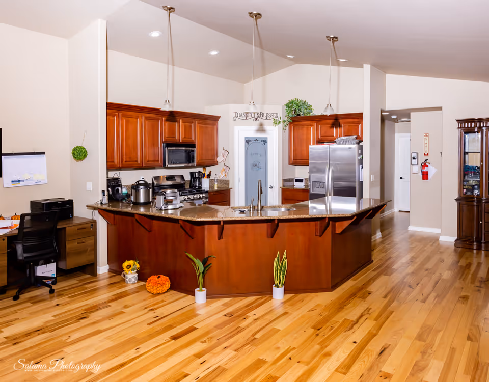 Open-concept kitchen with island, wooden cabinets, and stainless appliances in a senior living facility.
