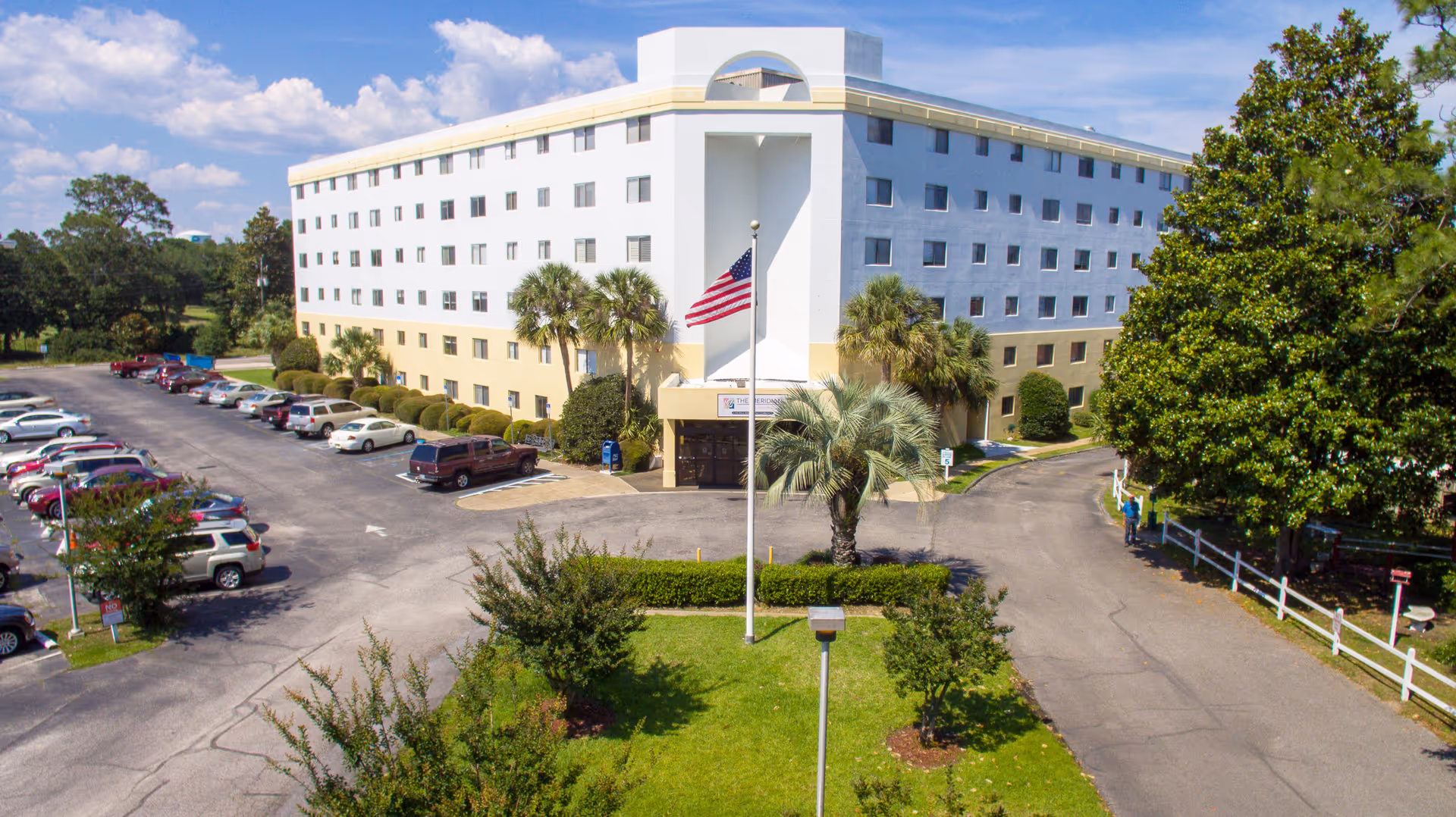 A large white multi-story senior living building with parked cars and a flagpole.
