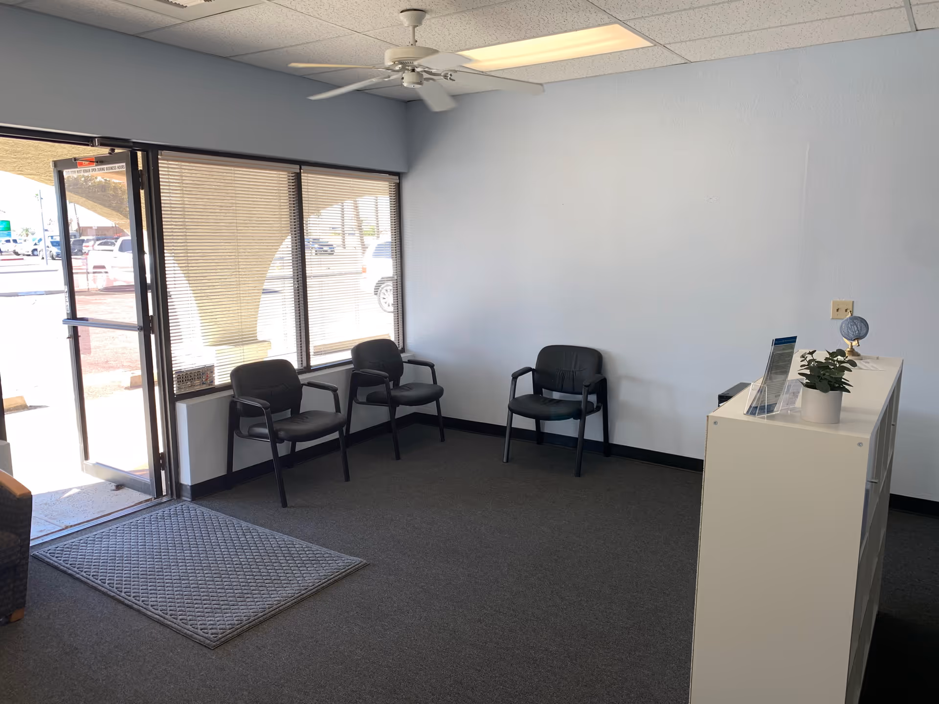Reception area with chairs, a front desk, and a large window by the glass entrance.
