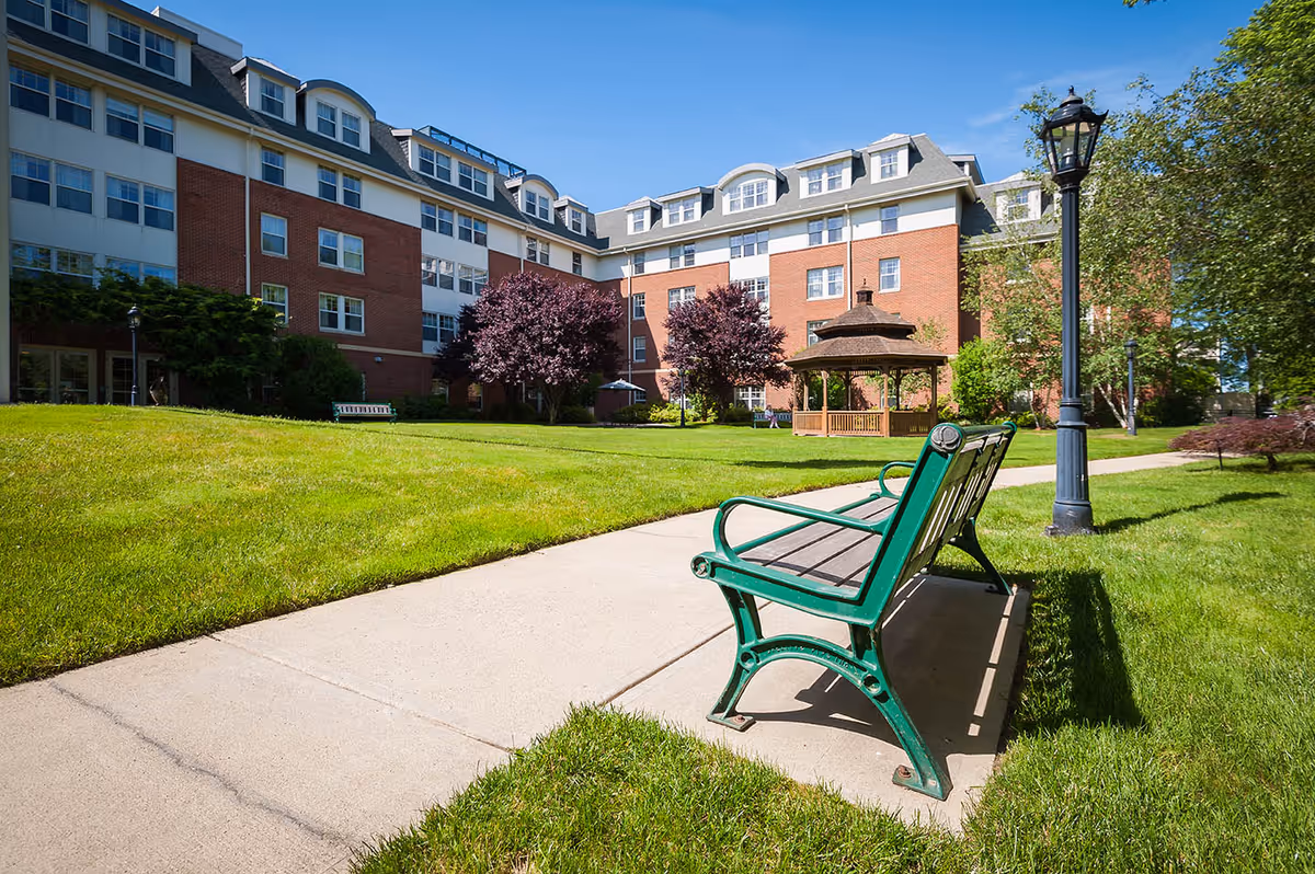 Blue-sky view of Providence House Assisted Living exterior with lawn, gazebo, and bench.