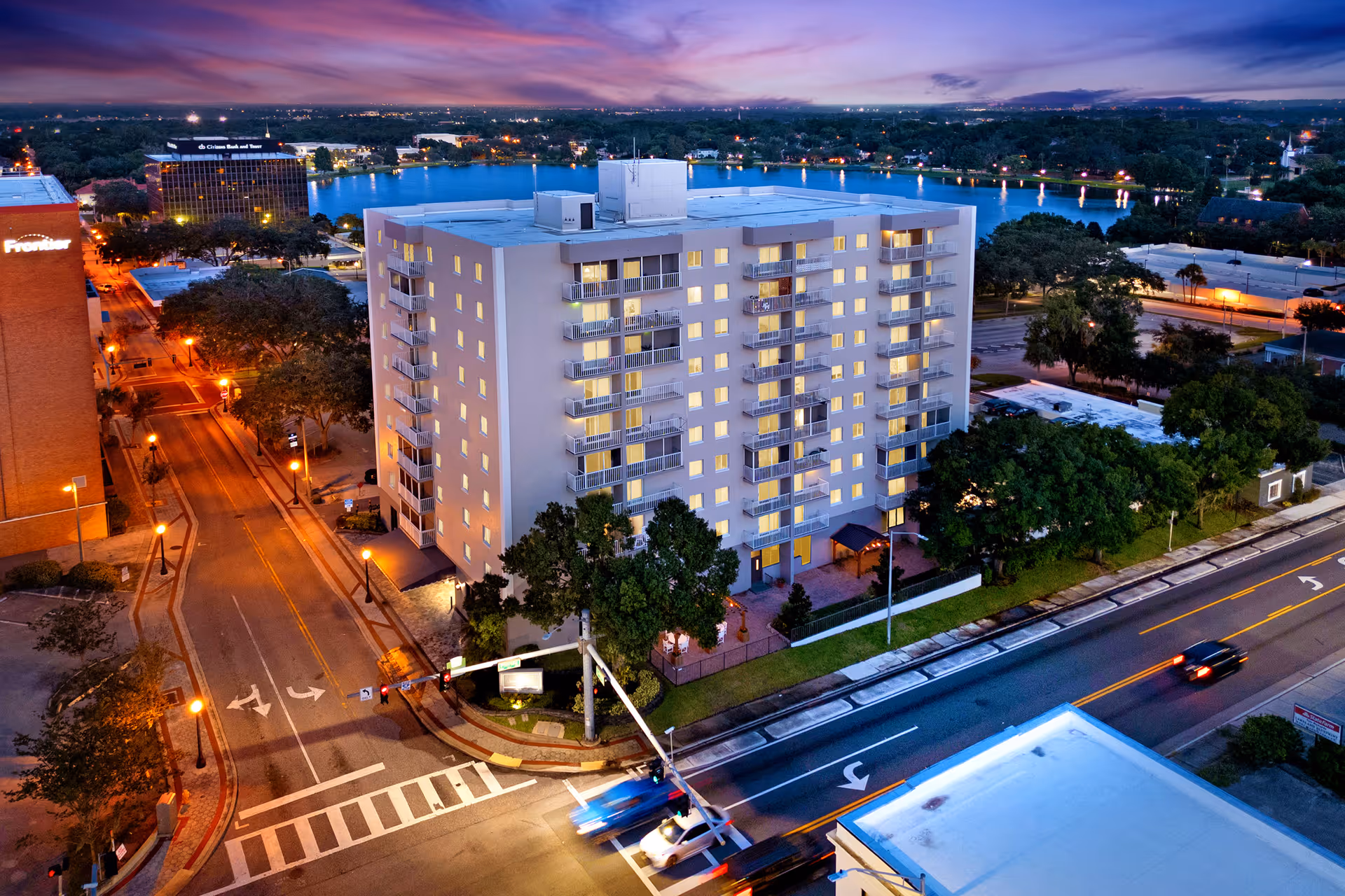 Aerial view of a high-rise residential building with streets and a lake in the background.