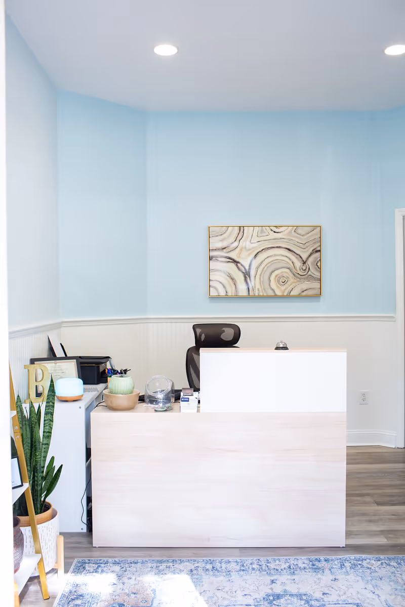 Bright reception area with light blue walls, a front desk, and decorative plants.
