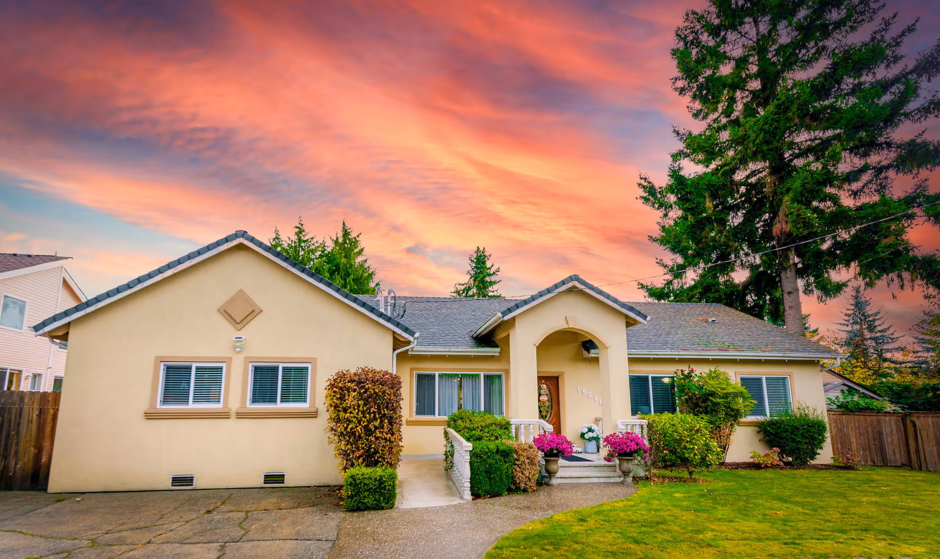 A single-story beige house with a small entryway and planters in a front yard at sunset.