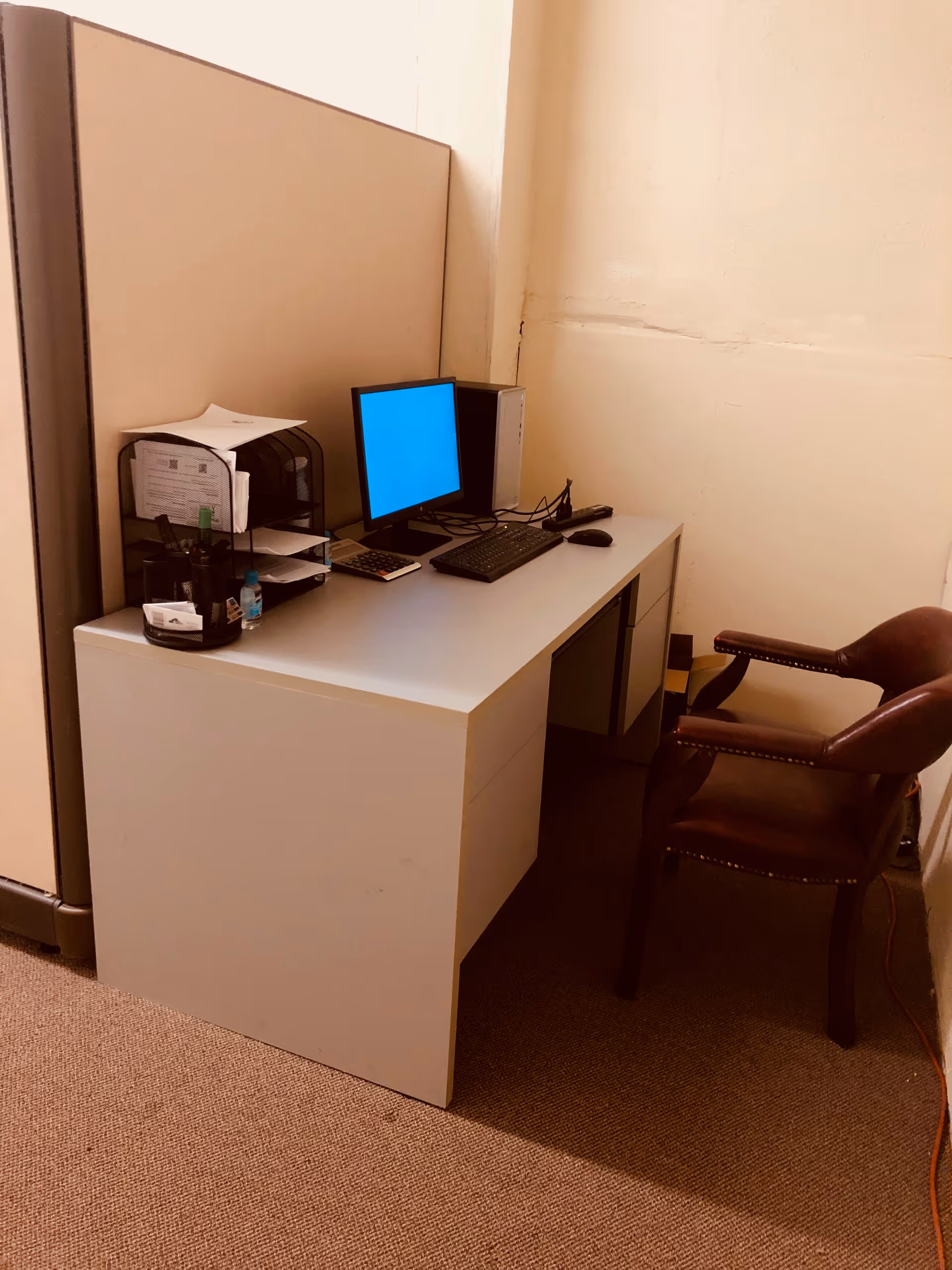 White desk with computer, papers, and a brown chair in a small office.