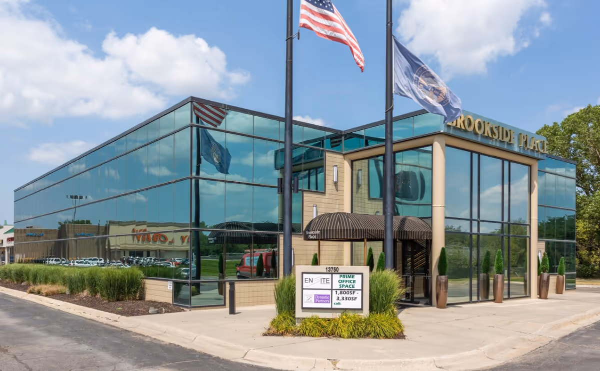 Glass-front building with flagpoles, curved entrance awning, and manicured shrubs.