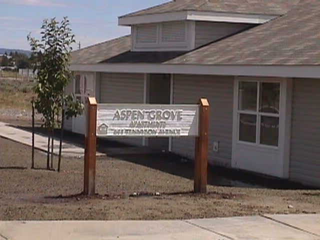 Single-story building exterior with a wooden Aspen Grove Apartments sign in front.