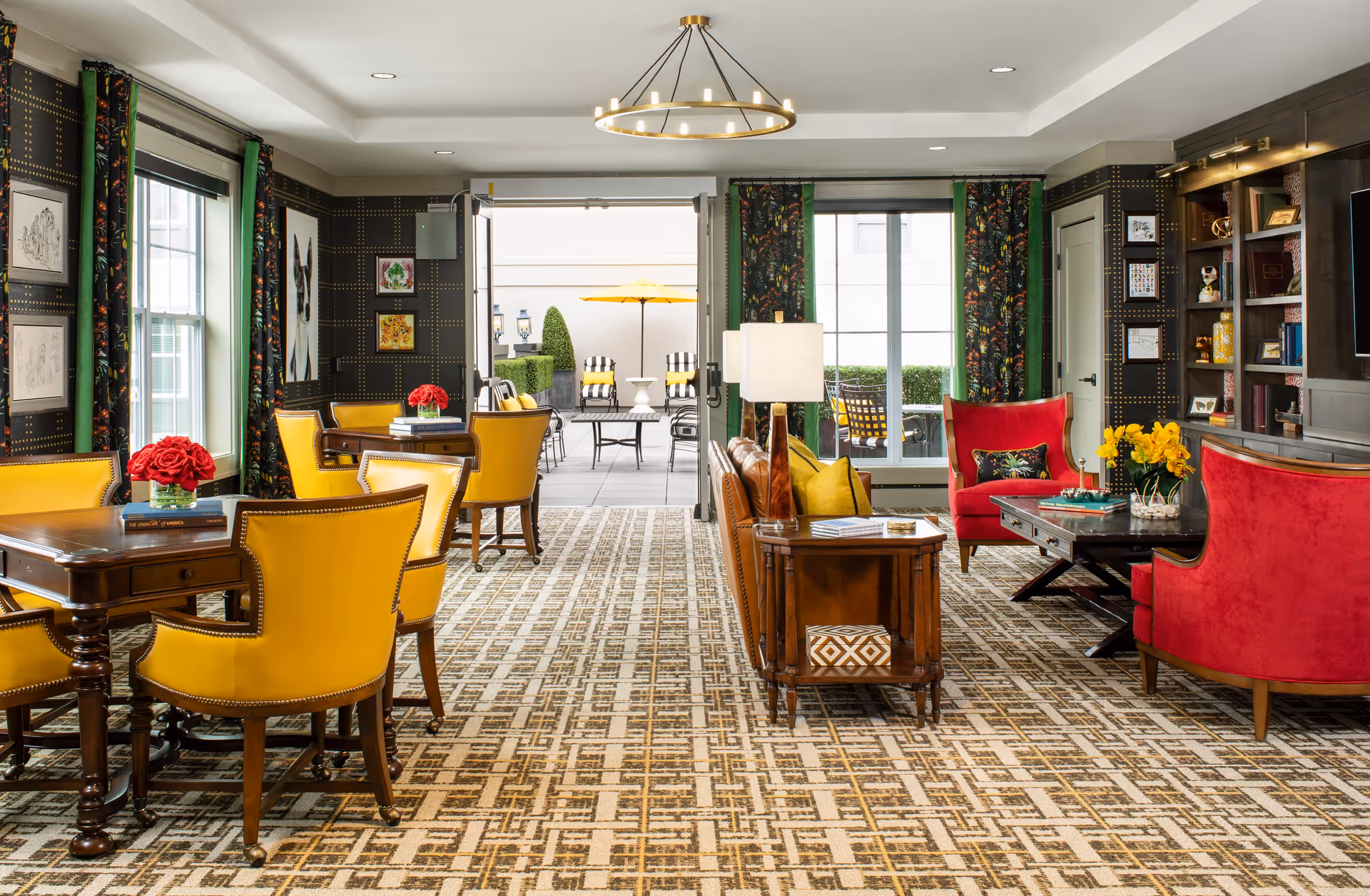 Bright communal lounge with yellow dining chairs, red armchairs, wood tables and an open doorway to an outdoor patio.