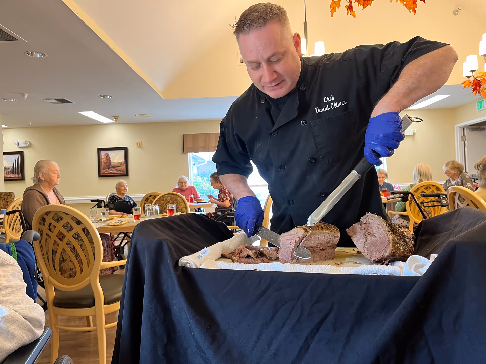 Chef carves roasted meat for residents at a dining room event in a senior living facility.