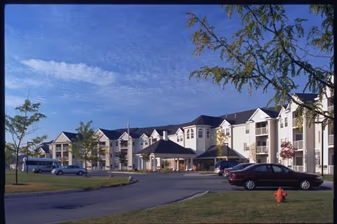 Exterior view of Grandhaven Manor senior living campus with parked cars and trees.