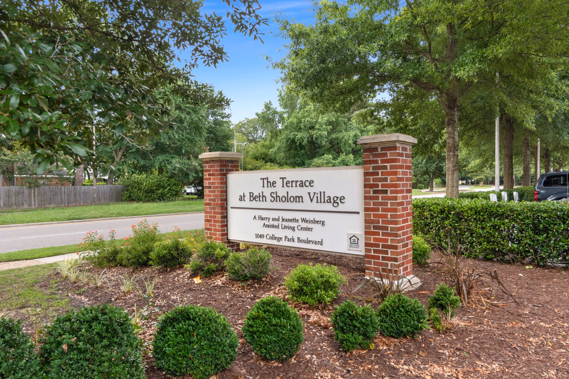 Entrance sign reading 'The Terrace at Beth Sholom Village' mounted between brick pillars, surrounded by landscaping and trees.