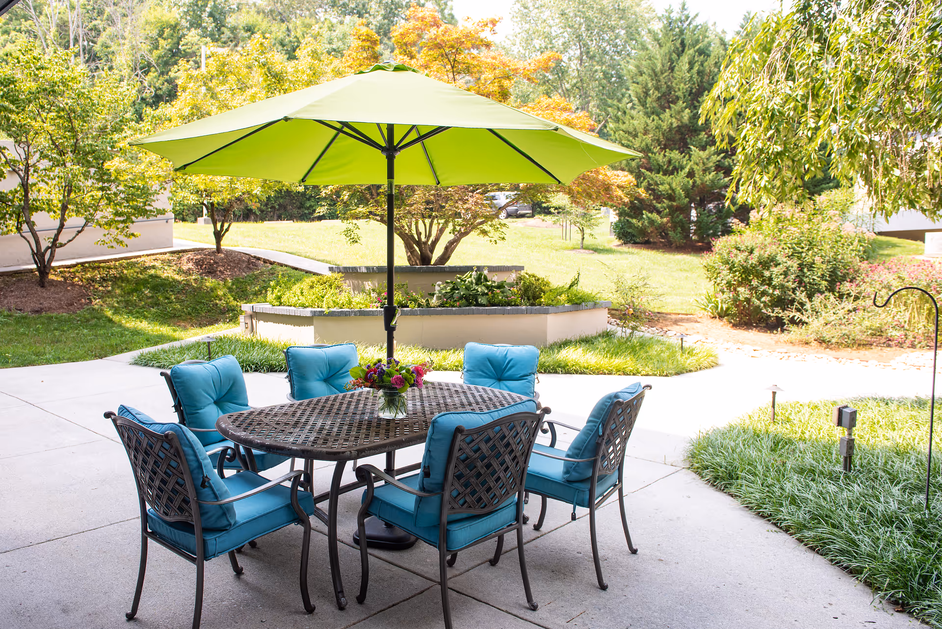 Outdoor patio with blue cushioned chairs and a green umbrella in a landscaped courtyard.