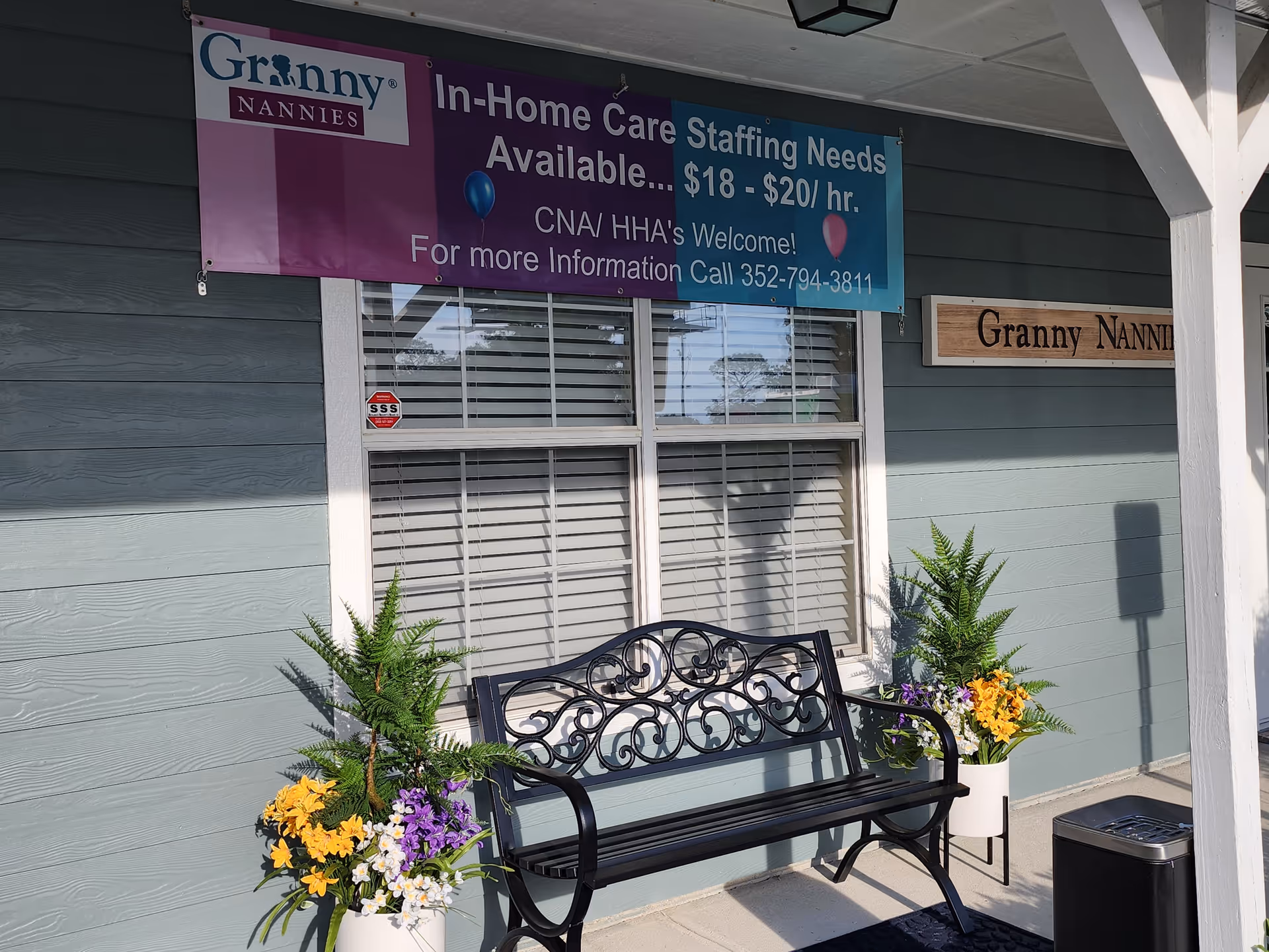 Exterior of Granny NANNIES facility with bench, banner, and potted flowers.