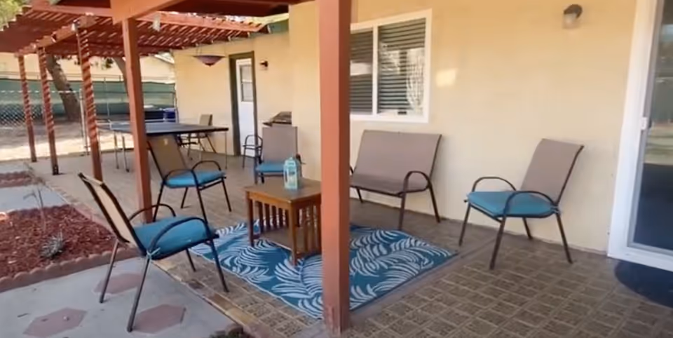 Outdoor covered patio with chairs, a small table, and a blue rug.