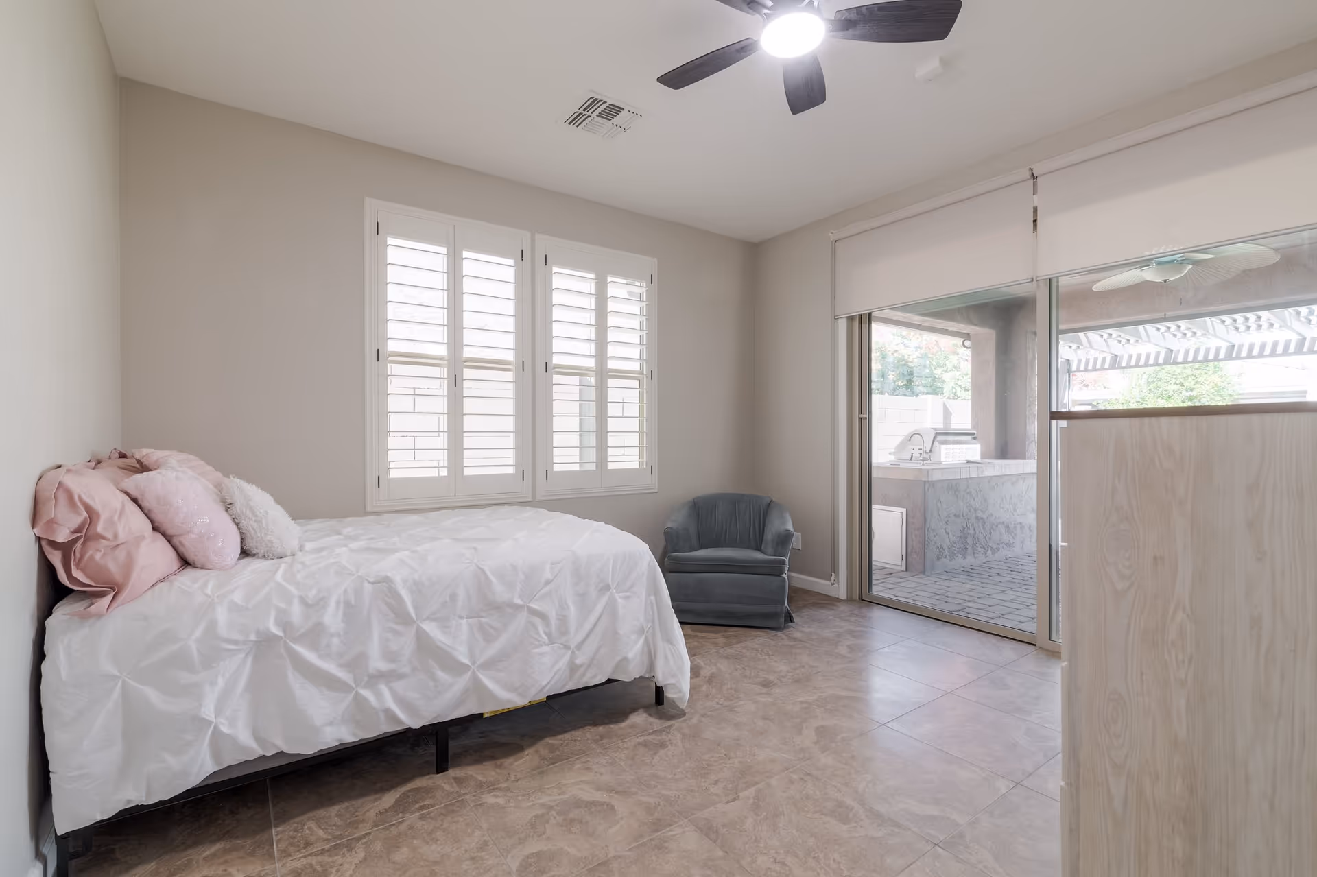 A clean bedroom with a bed, window shutters, and a glass door to an outdoor patio.