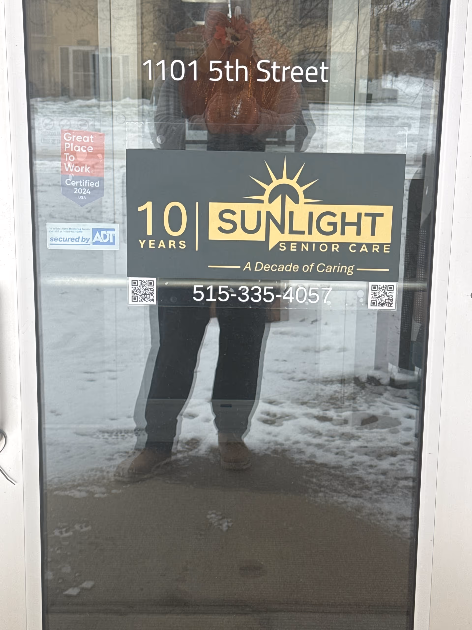 Glass door entrance with Sunlight Senior Care signage and a snowy reflection outside.