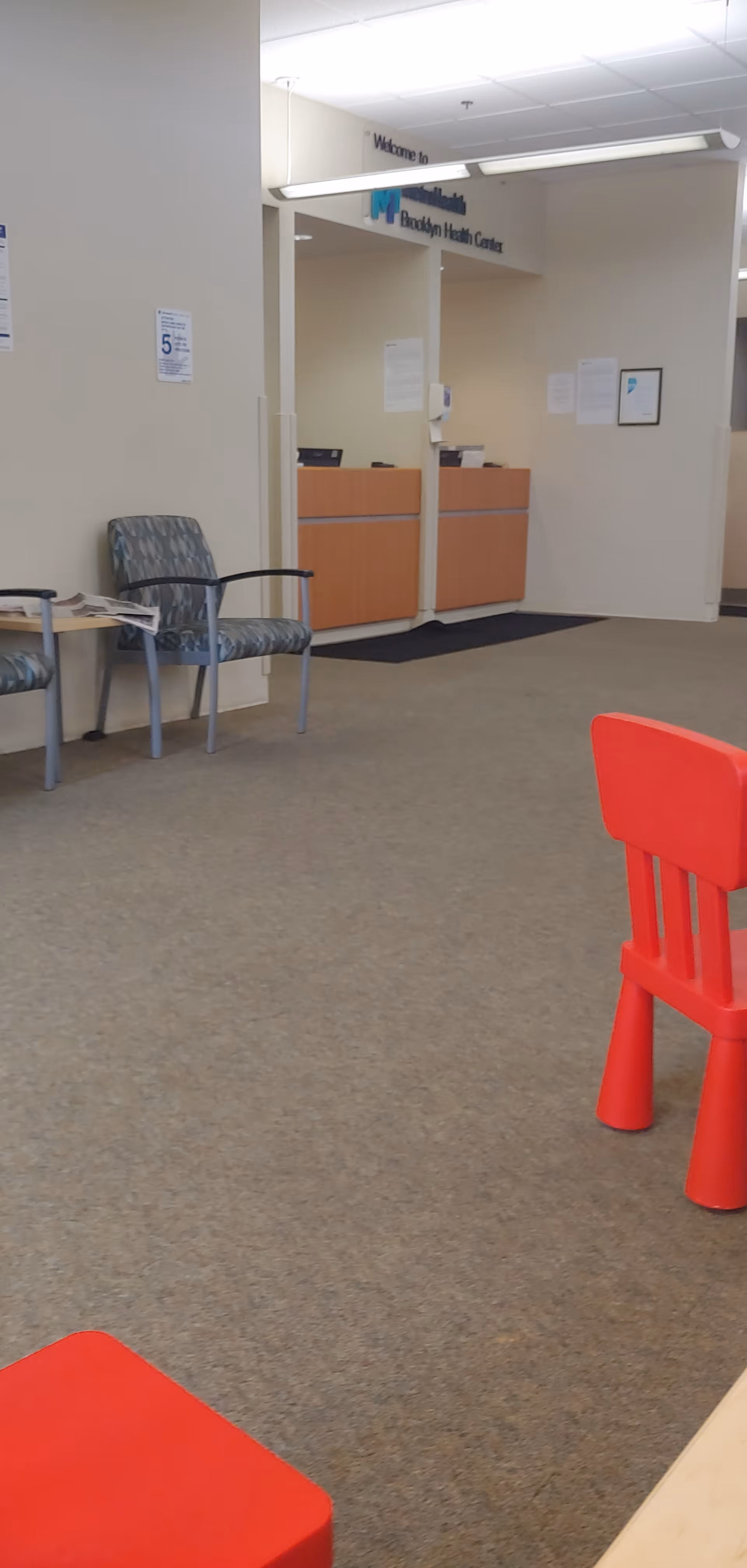 Reception area with chairs, a red plastic chair, and a desk at MetroHealth Brooklyn Health Center.