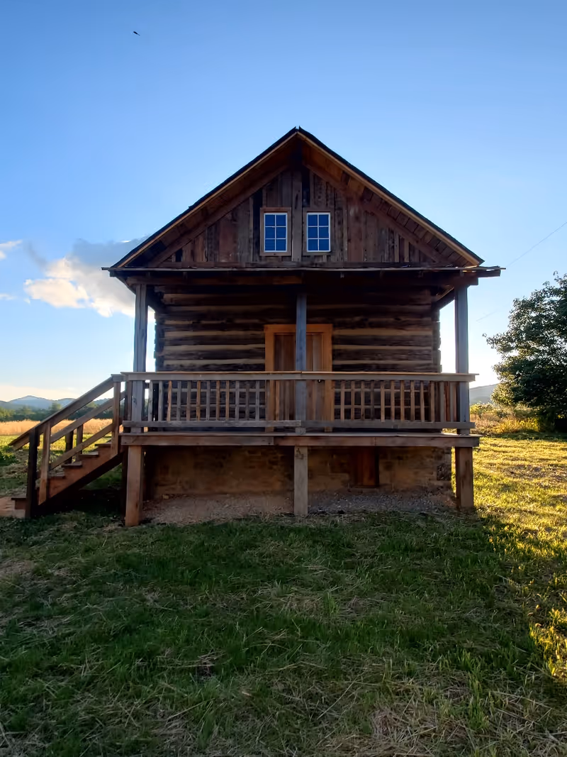 Rustic log cabin on a grassy field with a wooden staircase and porch.