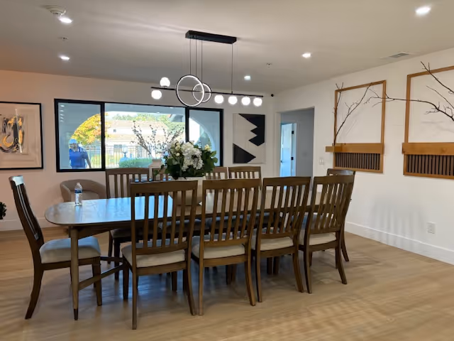 Spacious dining room with a long wooden table surrounded by multiple chairs beneath modern pendant lighting and wall decor.
