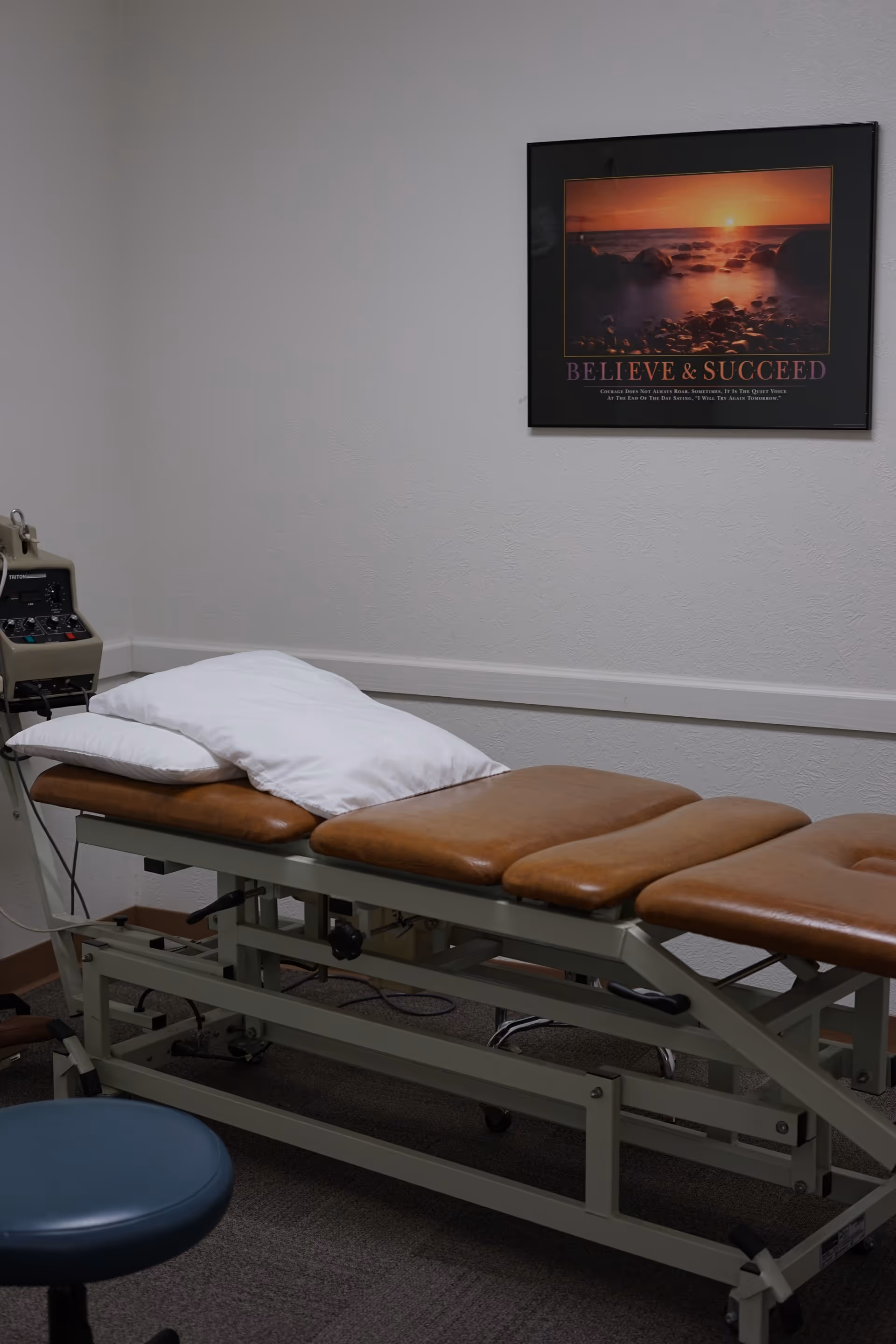 Therapy treatment table with pillow and medical equipment in a plain interior room.