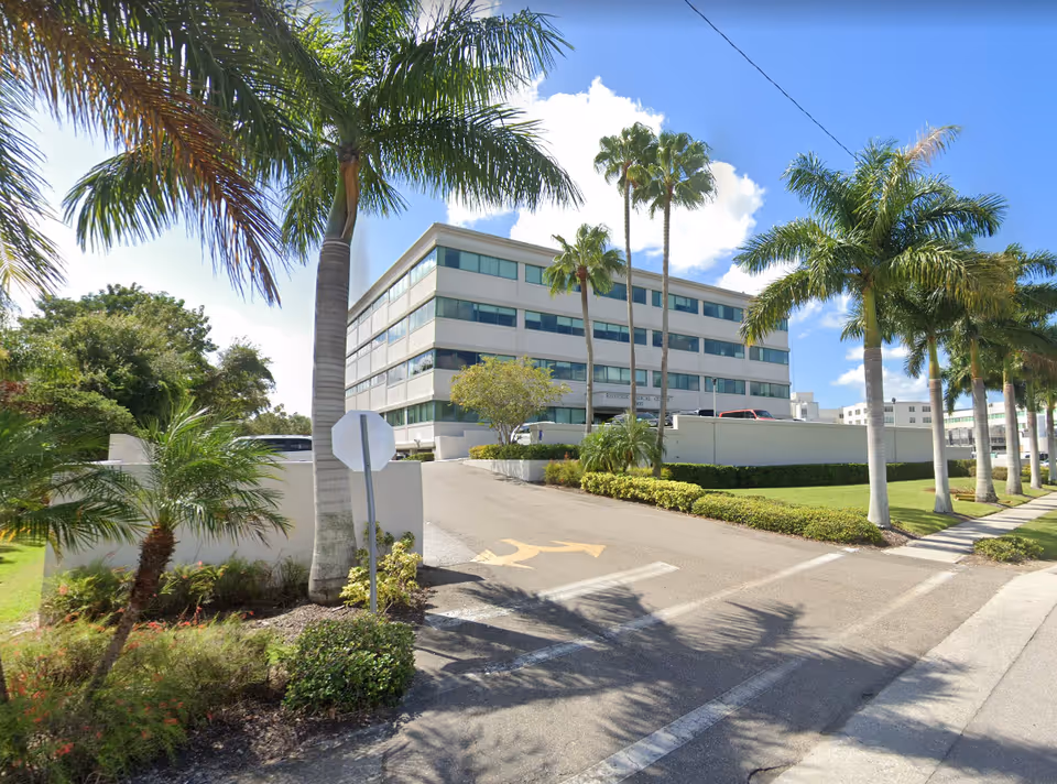 Modern four-story senior living building with palm trees and a driveway.
