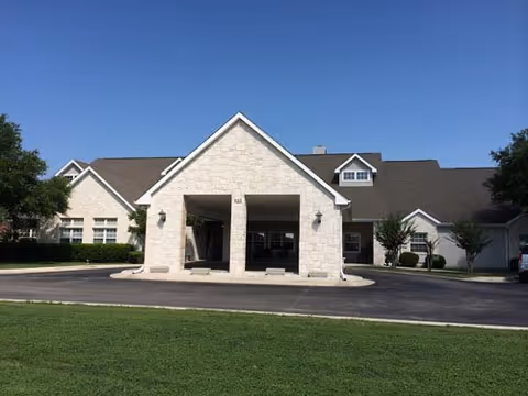 Stone-front entrance of Argent Court Assisted Living with a porte-cochère under a clear sky.