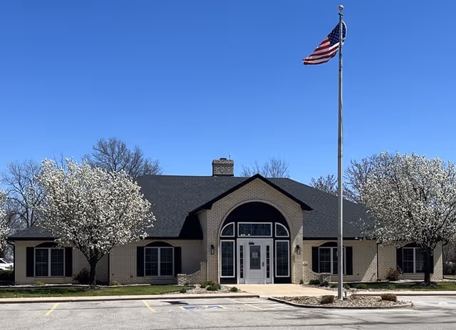 Front view of a single-story brick hospice with an arched central entrance and flagpole.