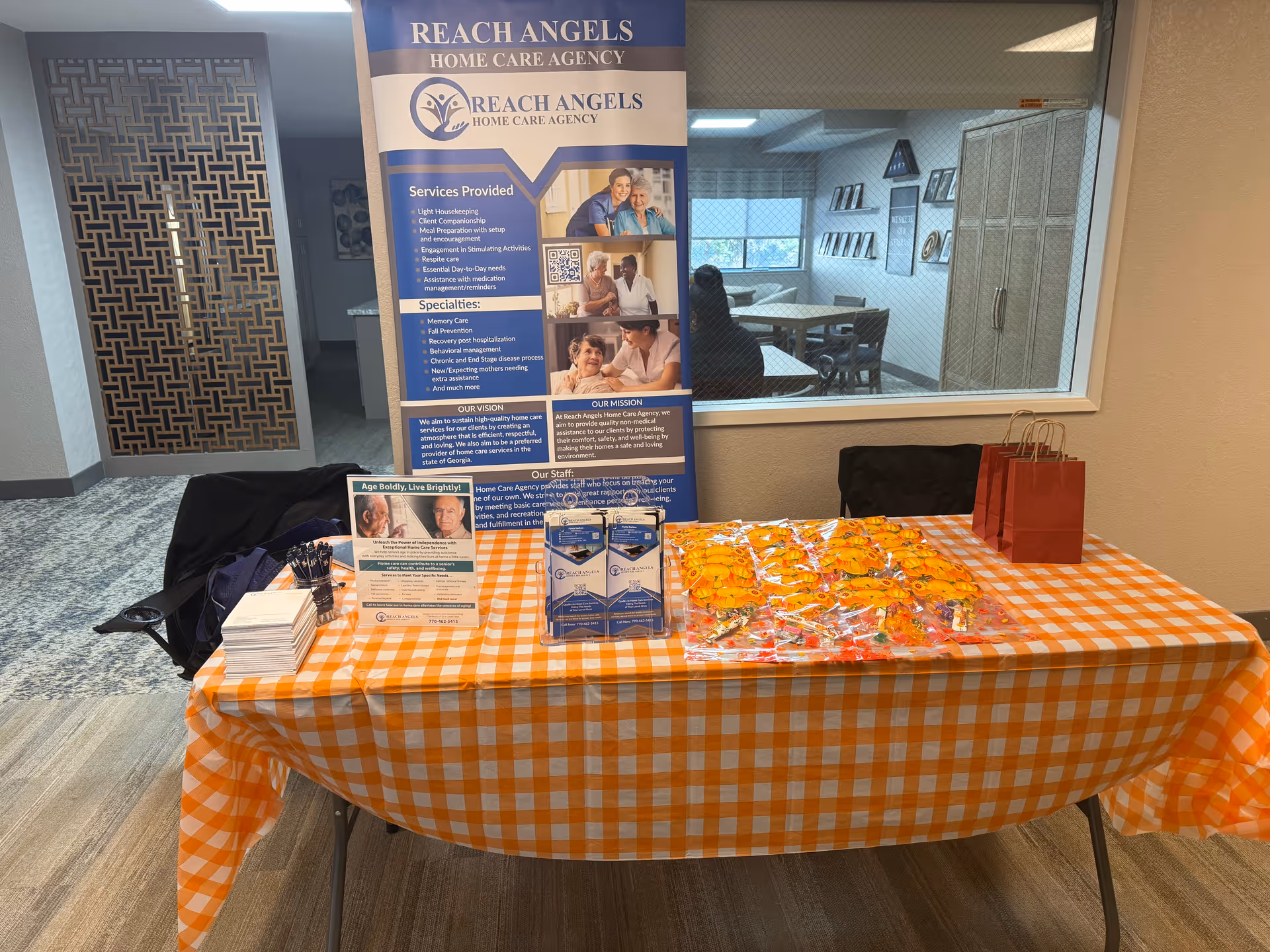 Promotional display with Reach Angels banner and orange-checkered tablecloth inside a facility lobby.