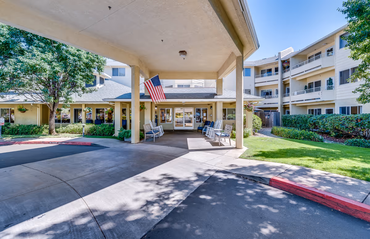 Front entrance of a senior living facility with a covered drop-off and seating area.