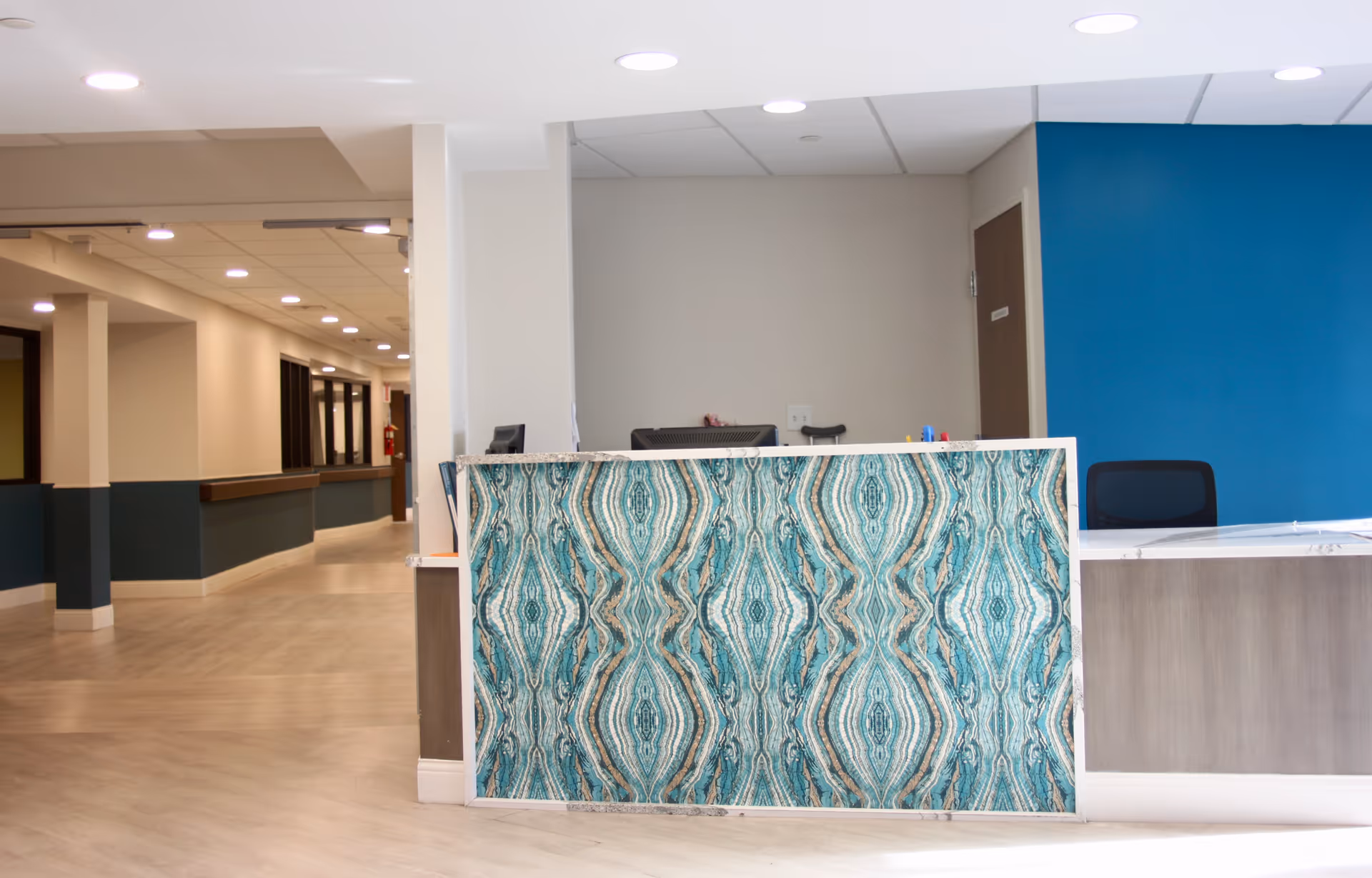 Reception desk with turquoise patterned panel in a bright interior hallway; blue wall behind.