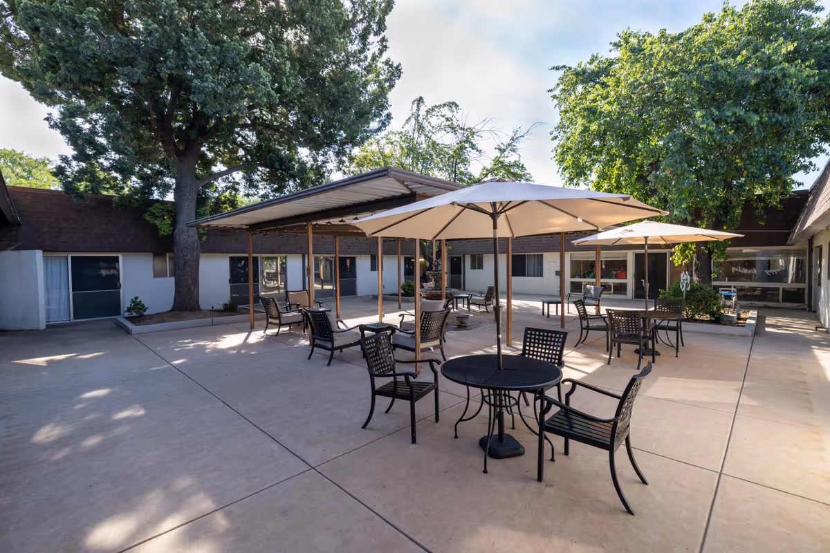 Outdoor courtyard with tables, chairs, and large umbrellas at a senior living facility.