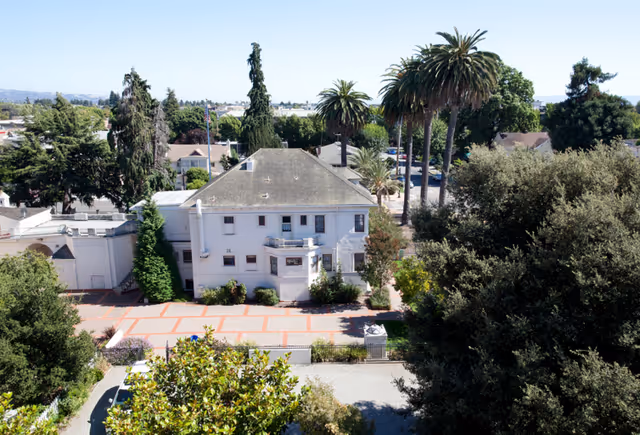 Aerial view of a white residential building with trees and a courtyard.